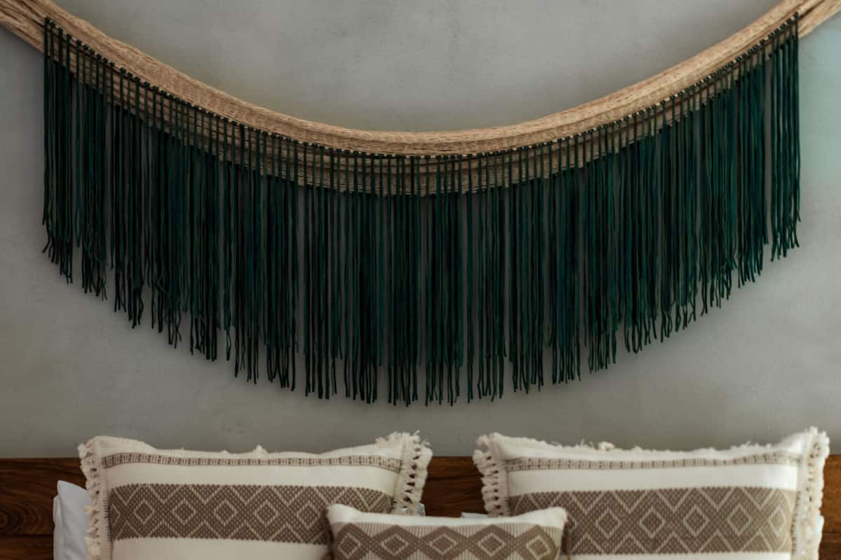 A bed with a woven headboard, a plain wall, and a bedspread with geometric patterned pillows.