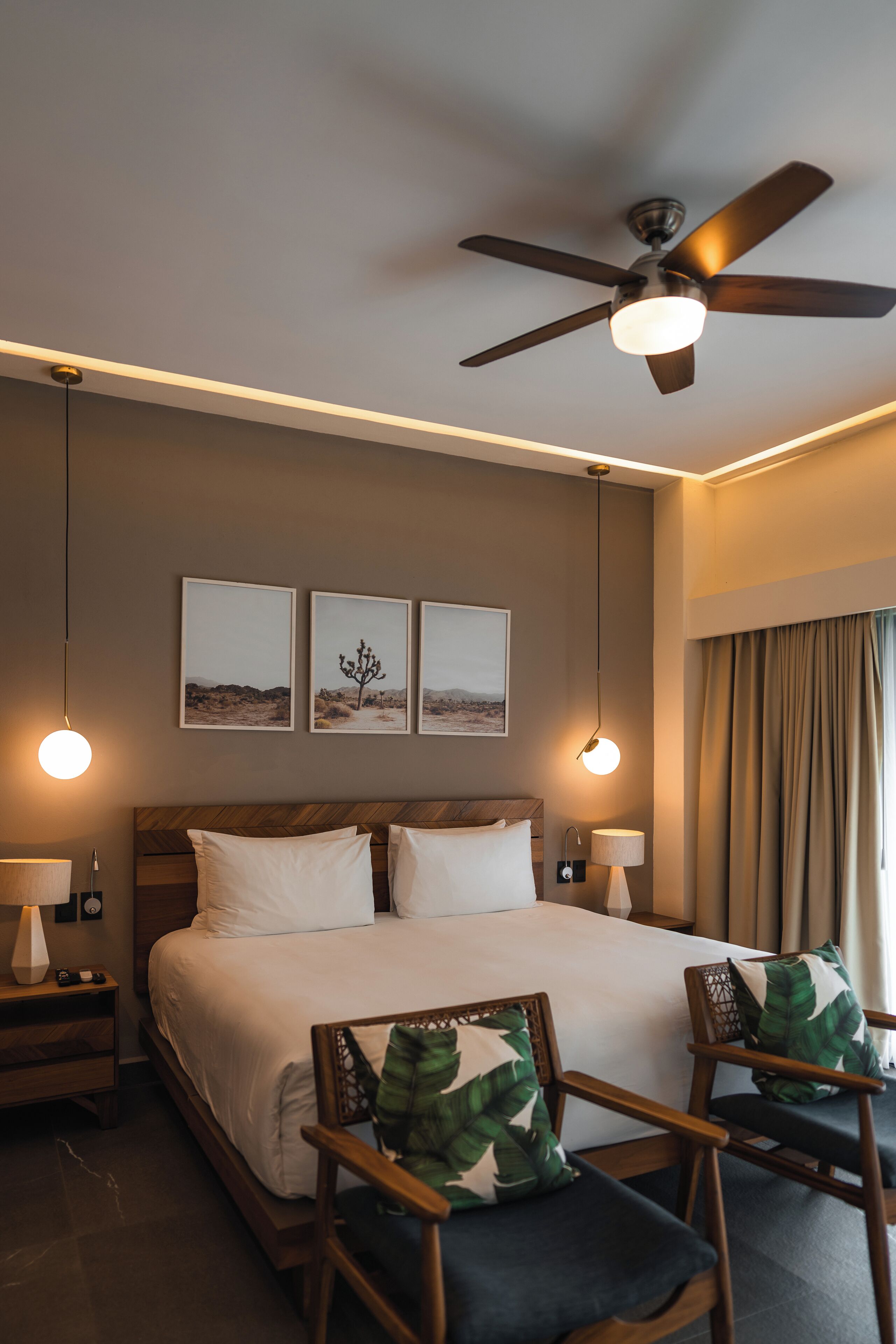 Ein Hotelzimmer mit einem Bett, zwei Stühlen, einem Deckenventilator und Wandbildern.