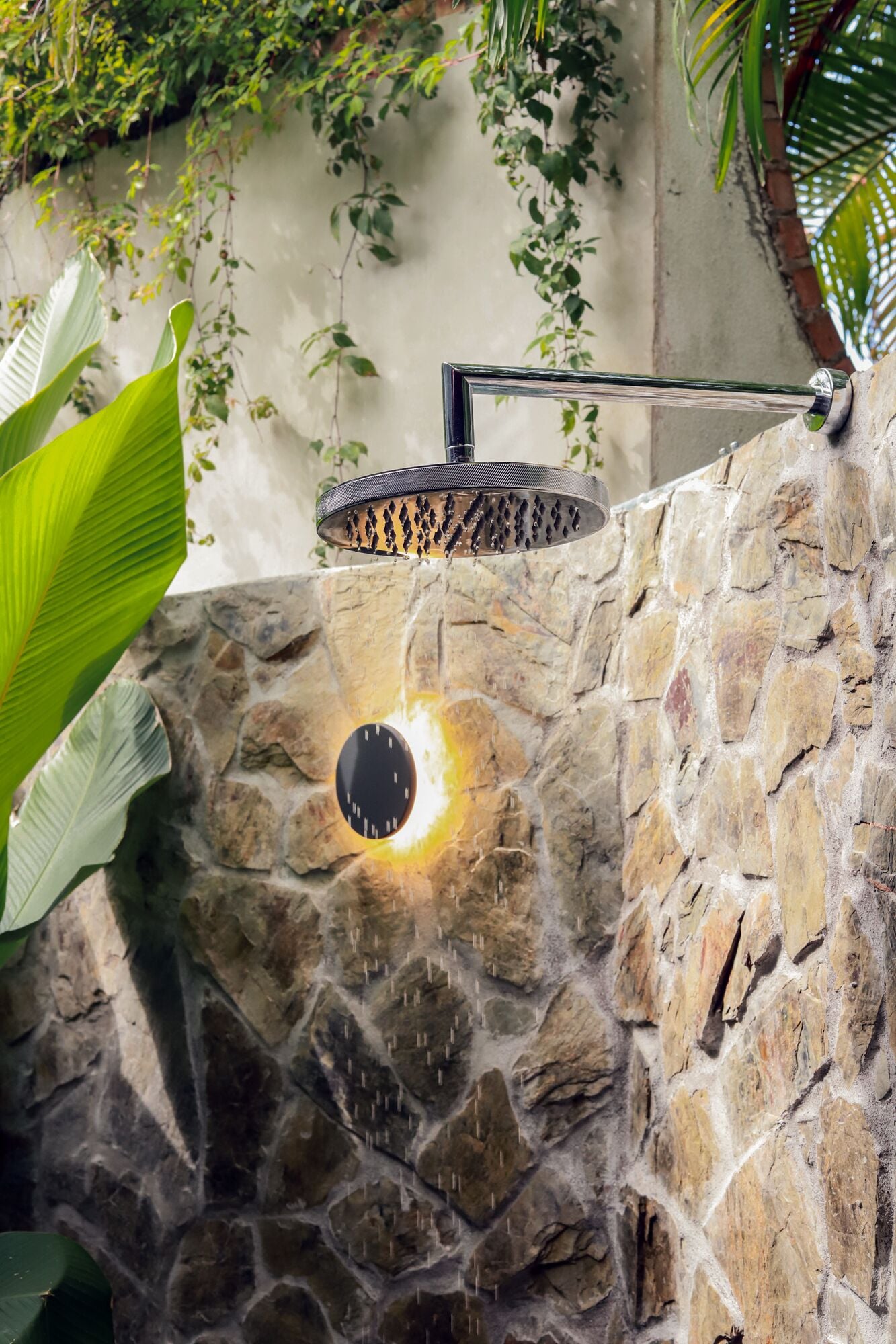 A stone wall with a built-in showerhead and a circular light fixture.