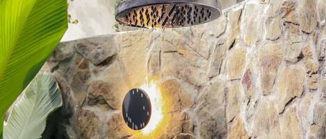 A stone wall with a built-in showerhead and a circular light fixture.