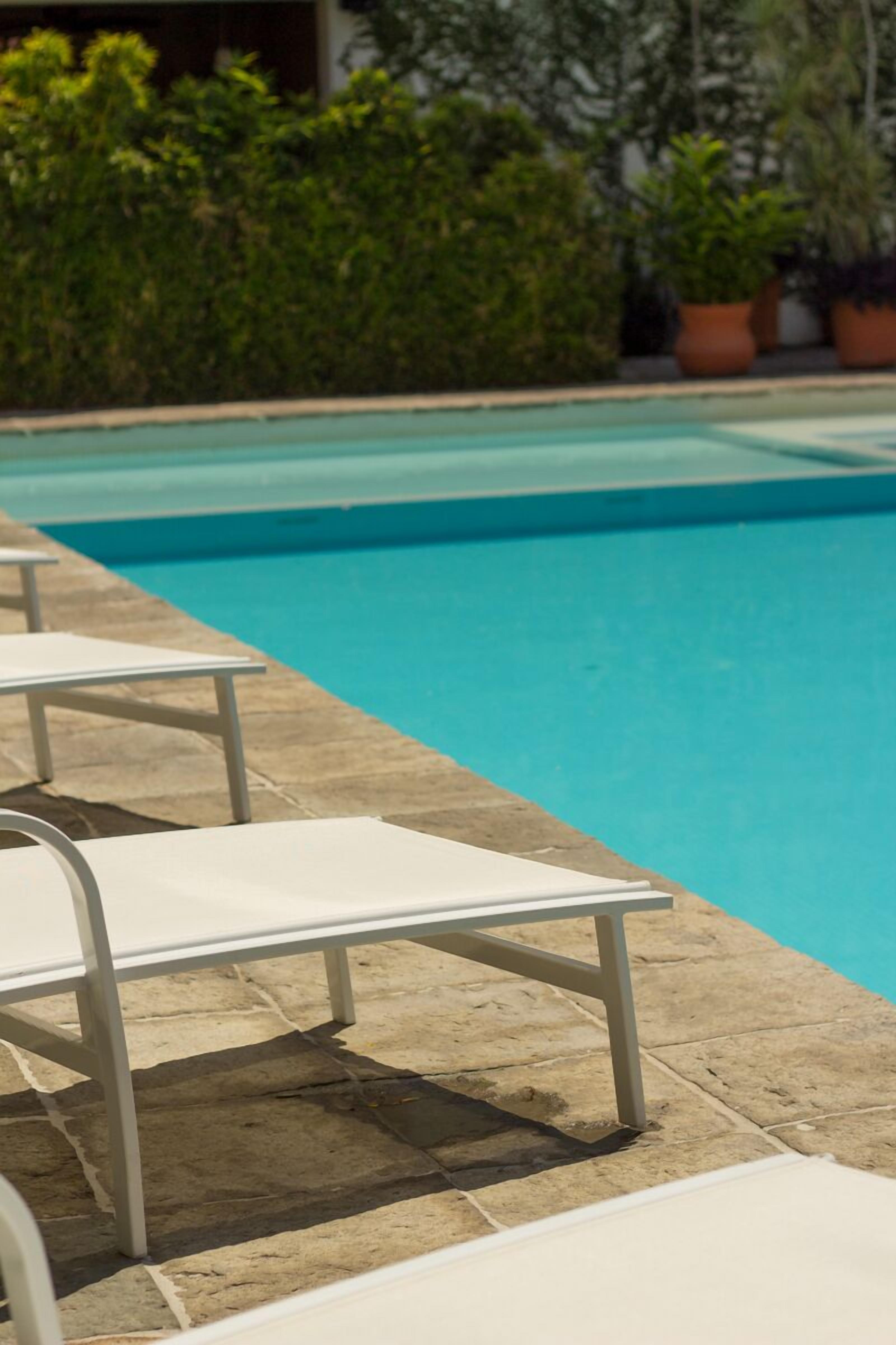 Ein Schwimmbecken mit weißen Liegestühlen und Pflanzen im Hintergrund.