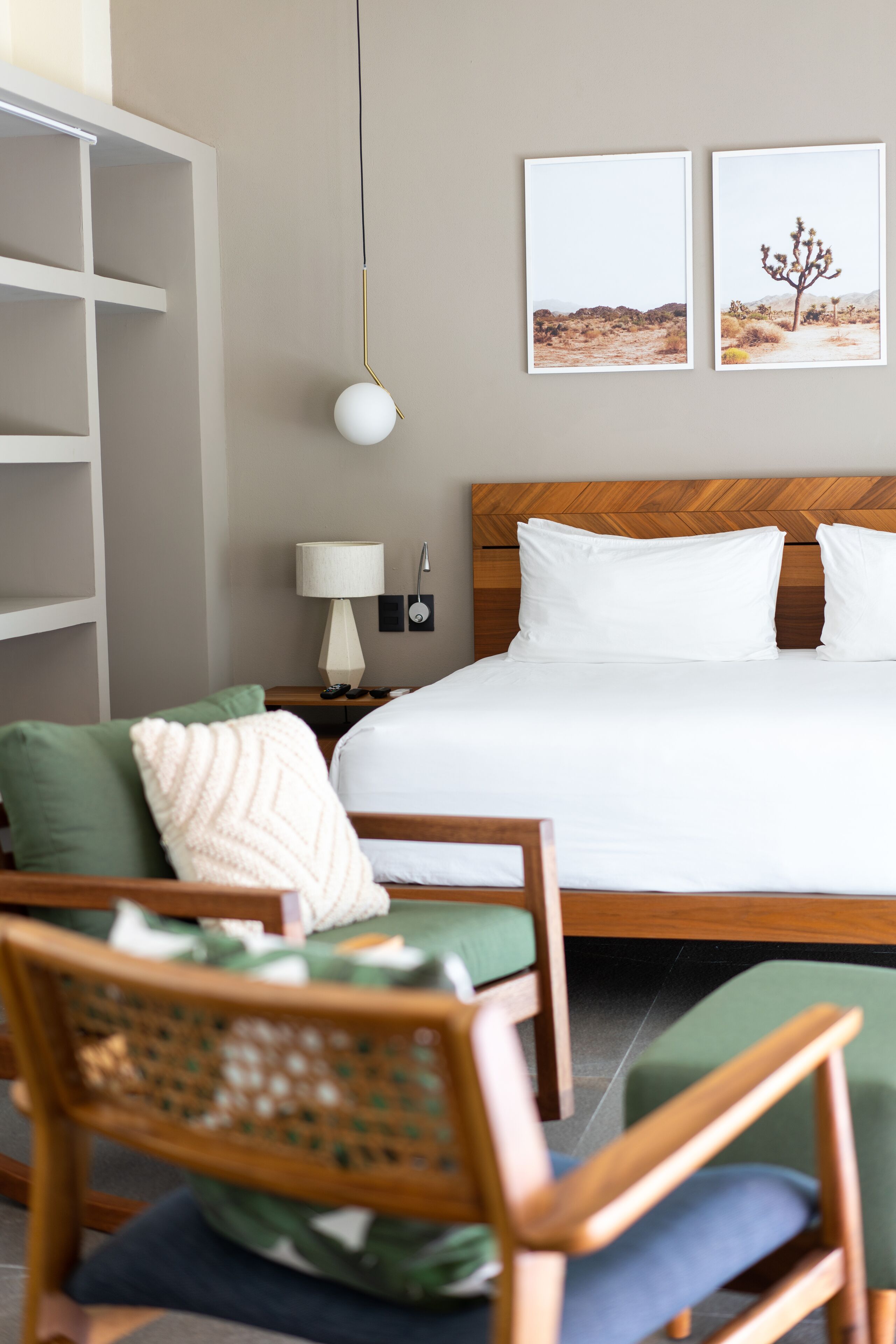 Un dormitorio ordenado con una cama grande, dos almohadas, una mesita de noche con una lámpara y dos cuadros enmarcados en la pared.