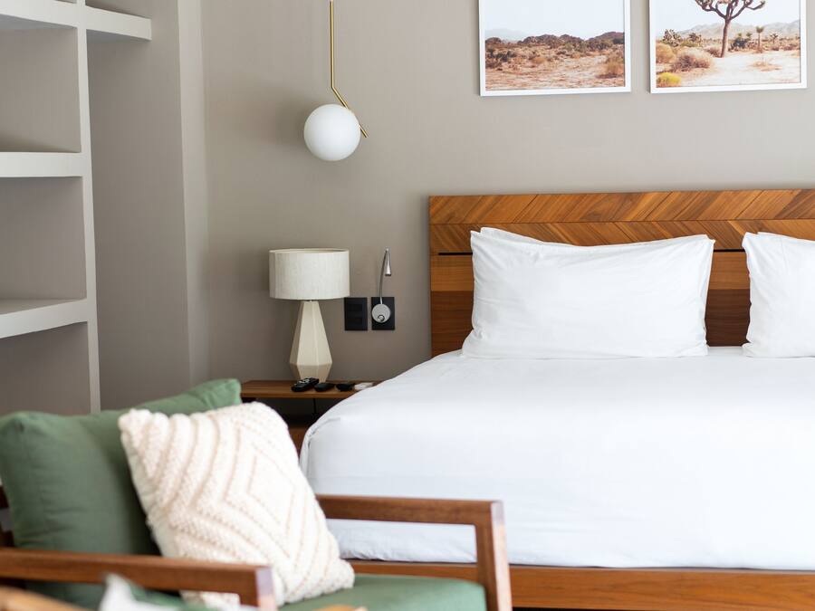 Un dormitorio ordenado con una cama grande, dos almohadas, una mesita de noche con una lámpara y dos cuadros enmarcados en la pared.