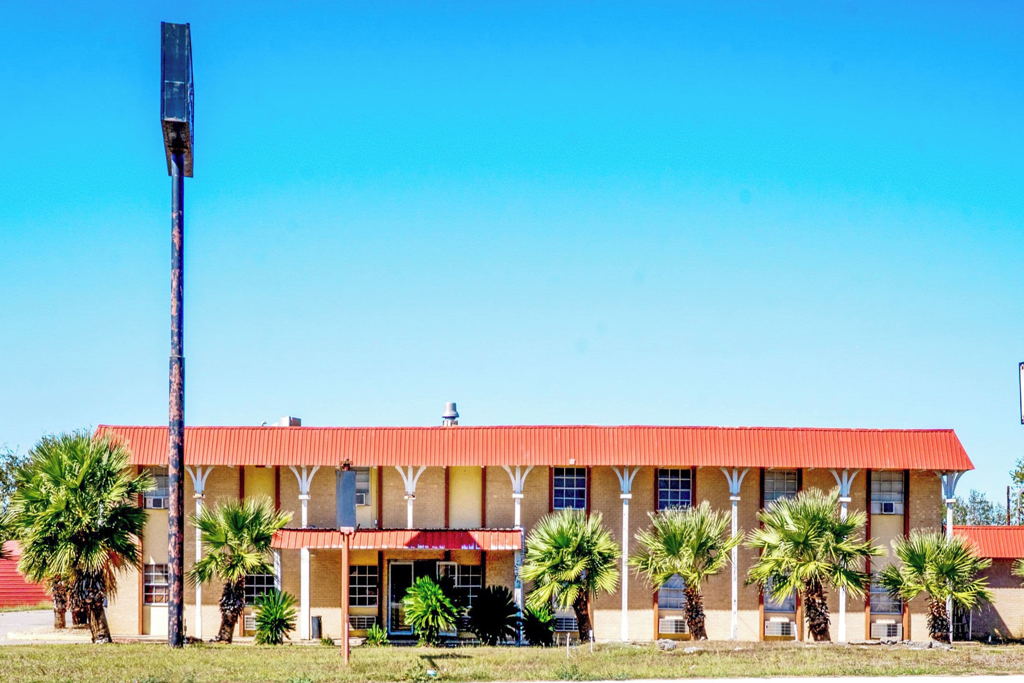 A building with a red roof and multiple windows, surrounded by palm trees.