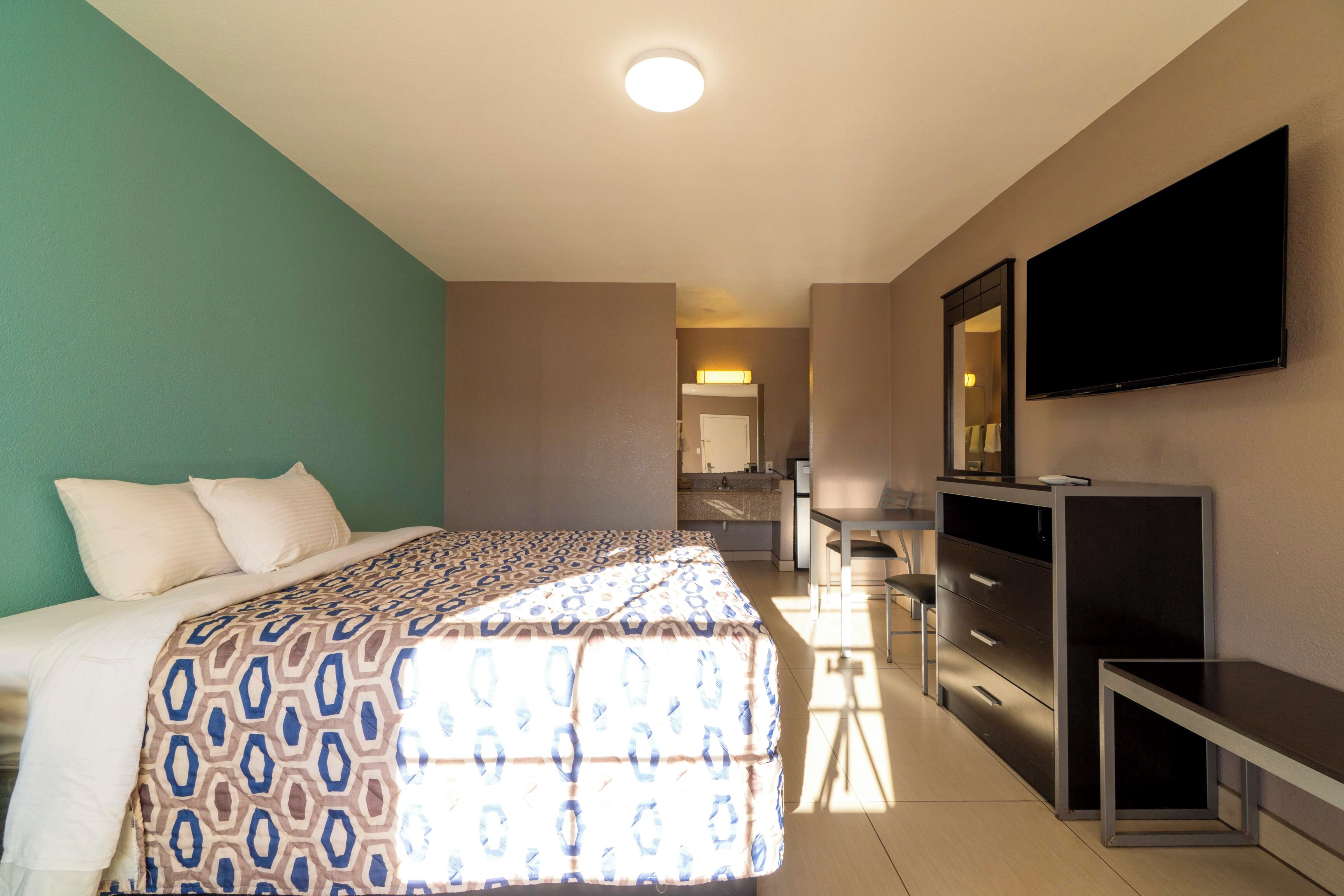 A hotel room with a bed, a desk, a television, and a bathroom visible in the background.