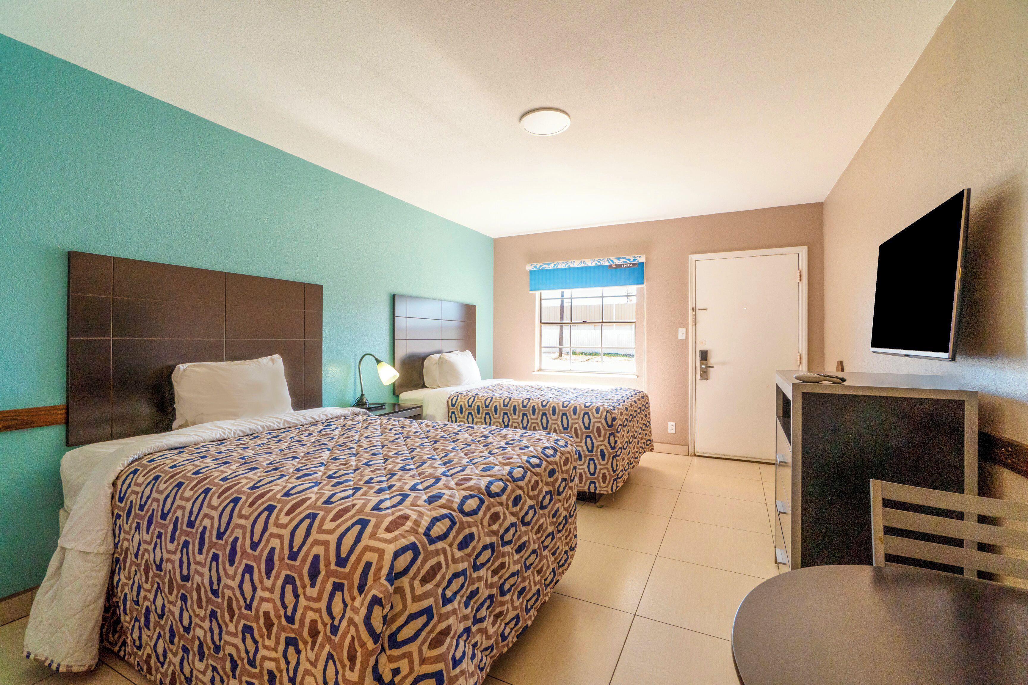 Habitación de hotel con dos camas, un escritorio, una silla y un televisor.