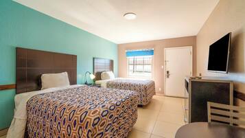 Habitación de hotel con dos camas, un escritorio, una silla y un televisor.
