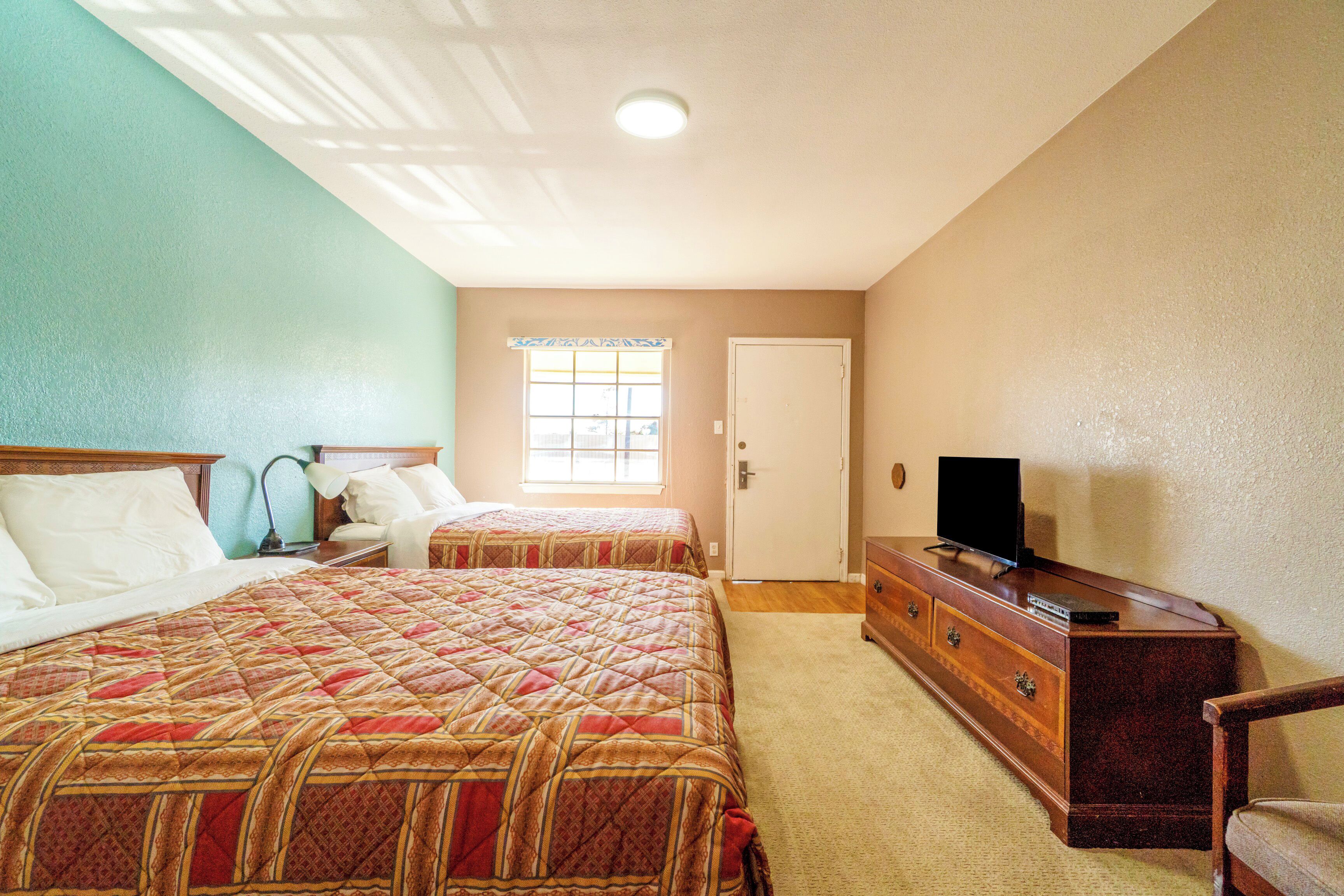 A bedroom with two beds, a dresser, a television, and a window.