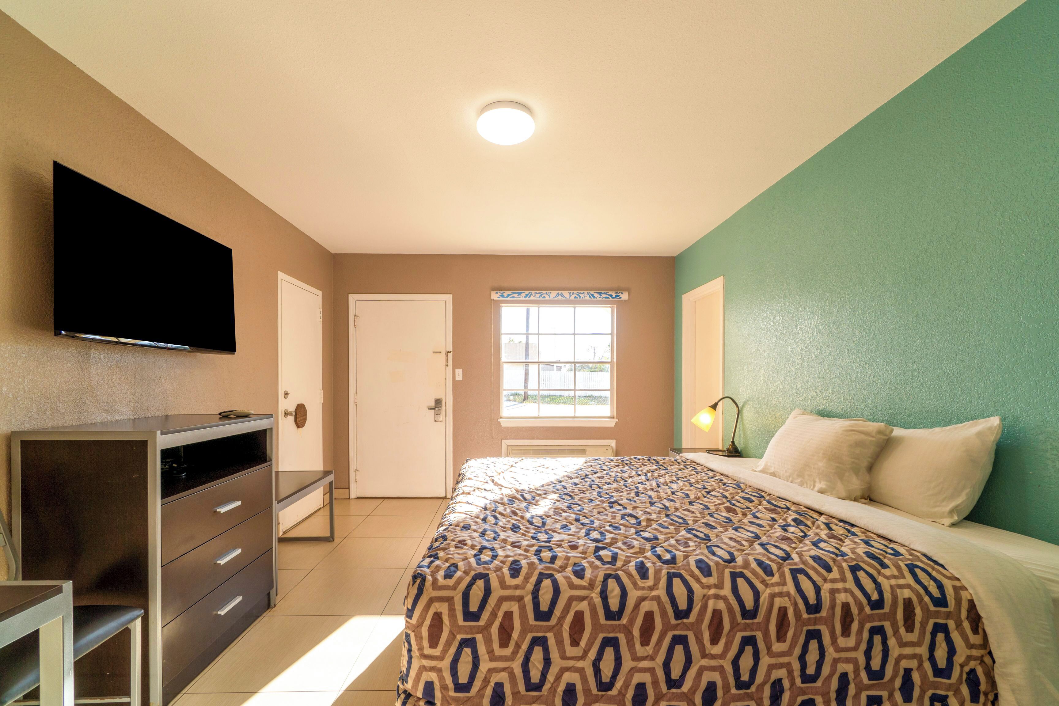 Un dormitorio con cama, cómoda, televisor y ventana con vistas.