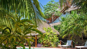 A pool area with lounge chairs, a thatched-roof structure, and tropical vegetation. - Holbox Deluxe Wellness Apartments (Isla Holbox)