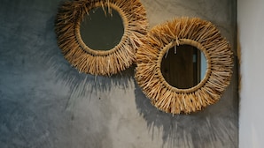 A bathroom with a large mirror, two circular woven wall decorations, a sink, a soap dispenser, a towel, and a tissue box. - Holbox Deluxe Wellness Apartments (Isla Holbox)