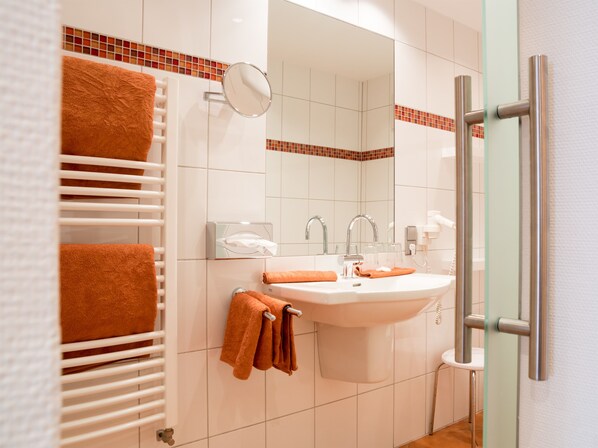 Un baño con un lavamanos blanco, dos grifos, un espejo y un toallero con toallas anaranjadas.