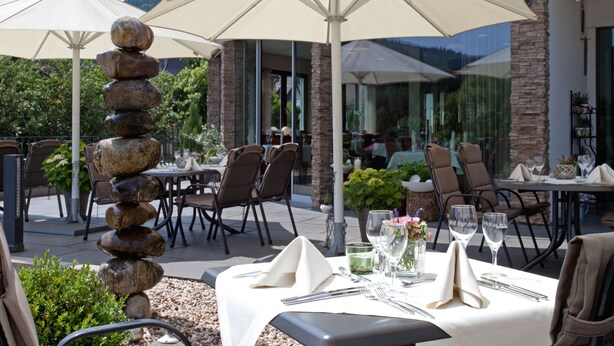 Un área de comedor al aire libre con mesas preparadas para dos, cubiertas por sombrillas grandes, y una pila de piedras como centro de mesa.