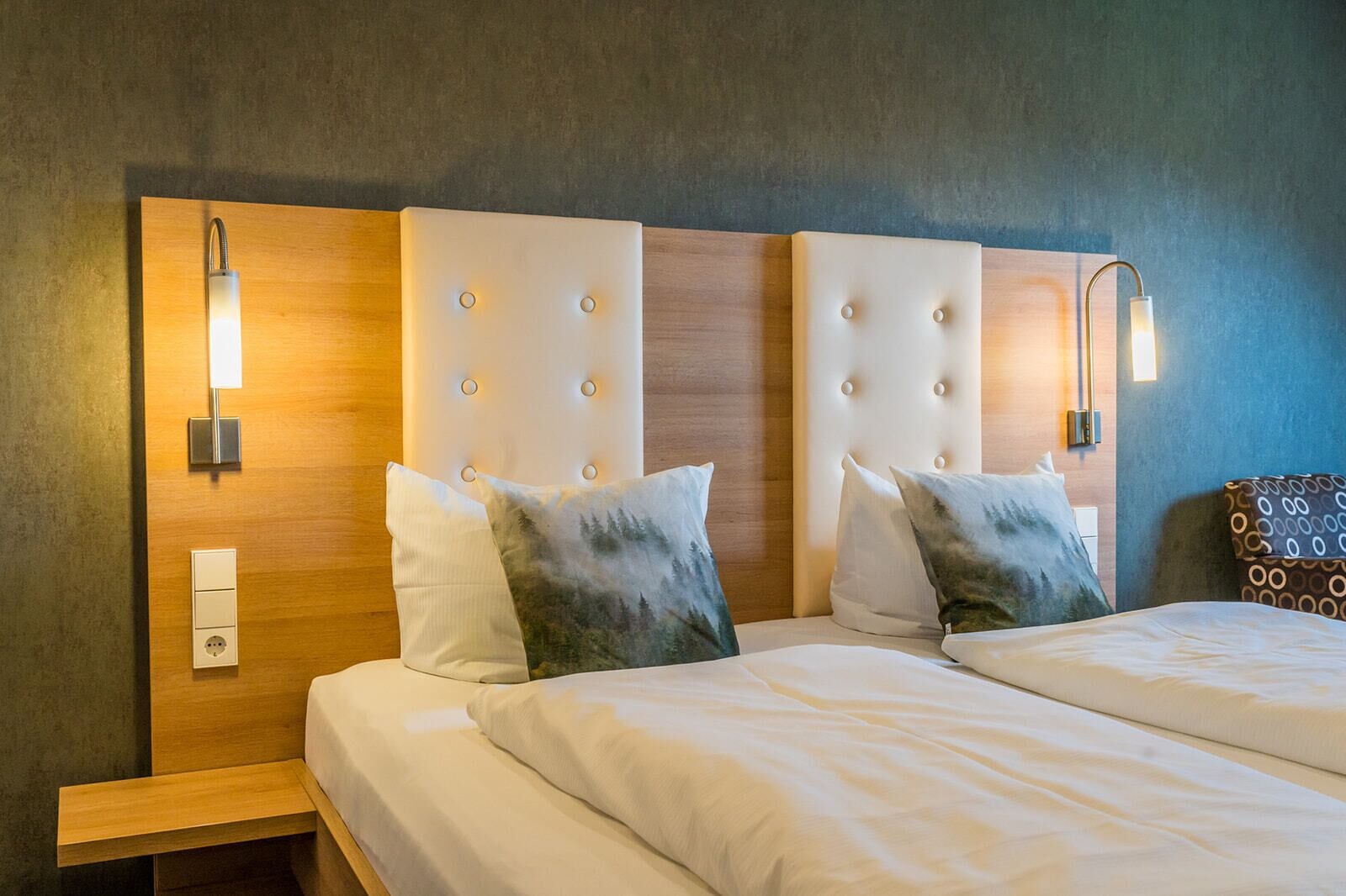 Una habitació d'hotel amb dos llits, ambres de fusta i aplics de paret.