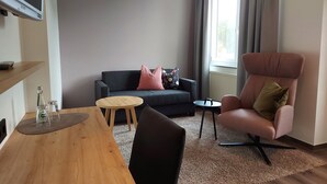 Una sala de estar moderna con un sofá gris oscuro, una mesa de centro de madera, un sillón rosa y una mesita auxiliar.