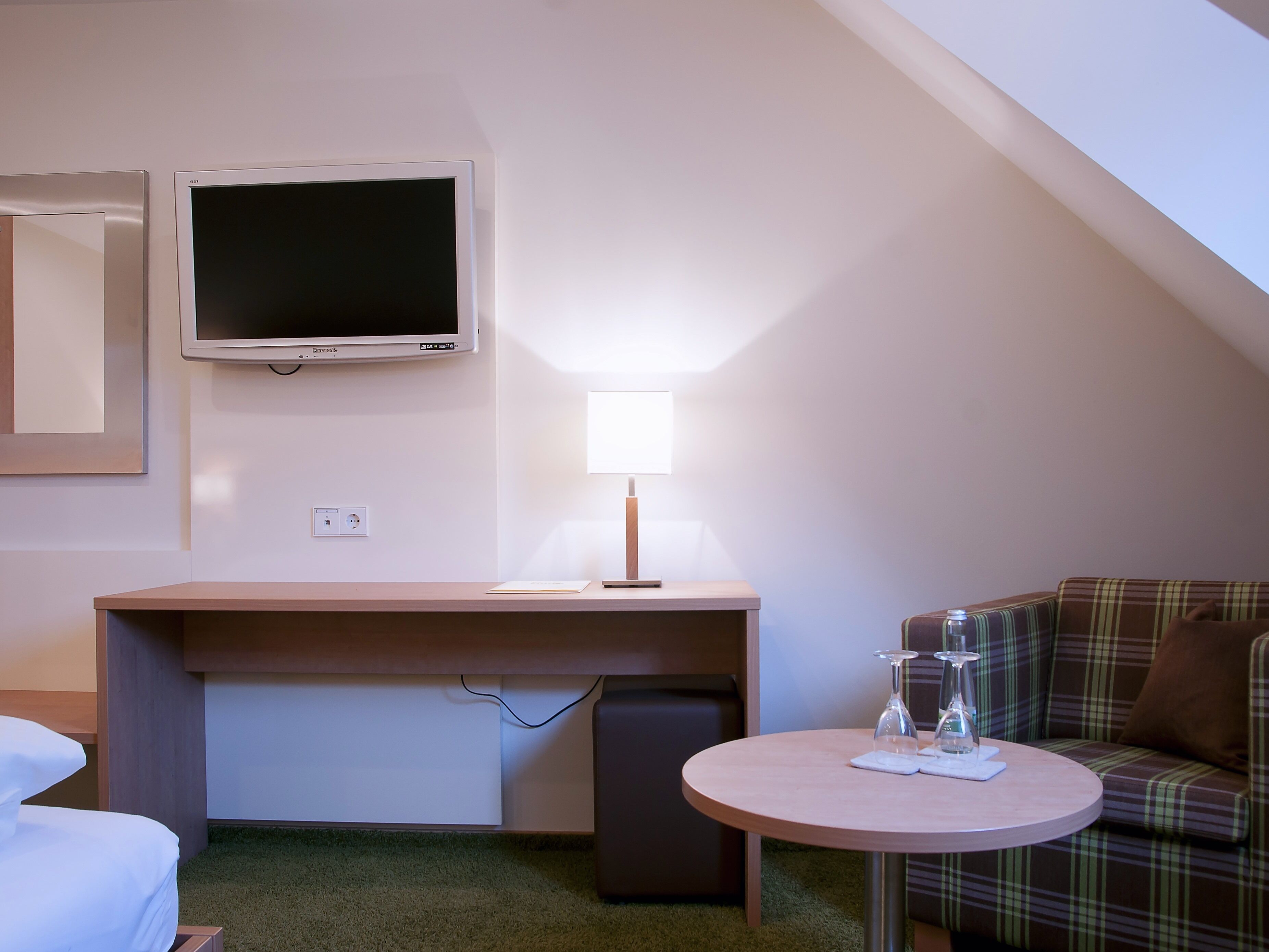 Hotelkamer met een bed, een bureau met een computer, een televisie, een lamp en een kleine ronde tafel met glazen.