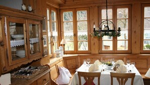 Comedor de madera con una mesa preparada para seis comensales, ventanas amplias y vistas al exterior.