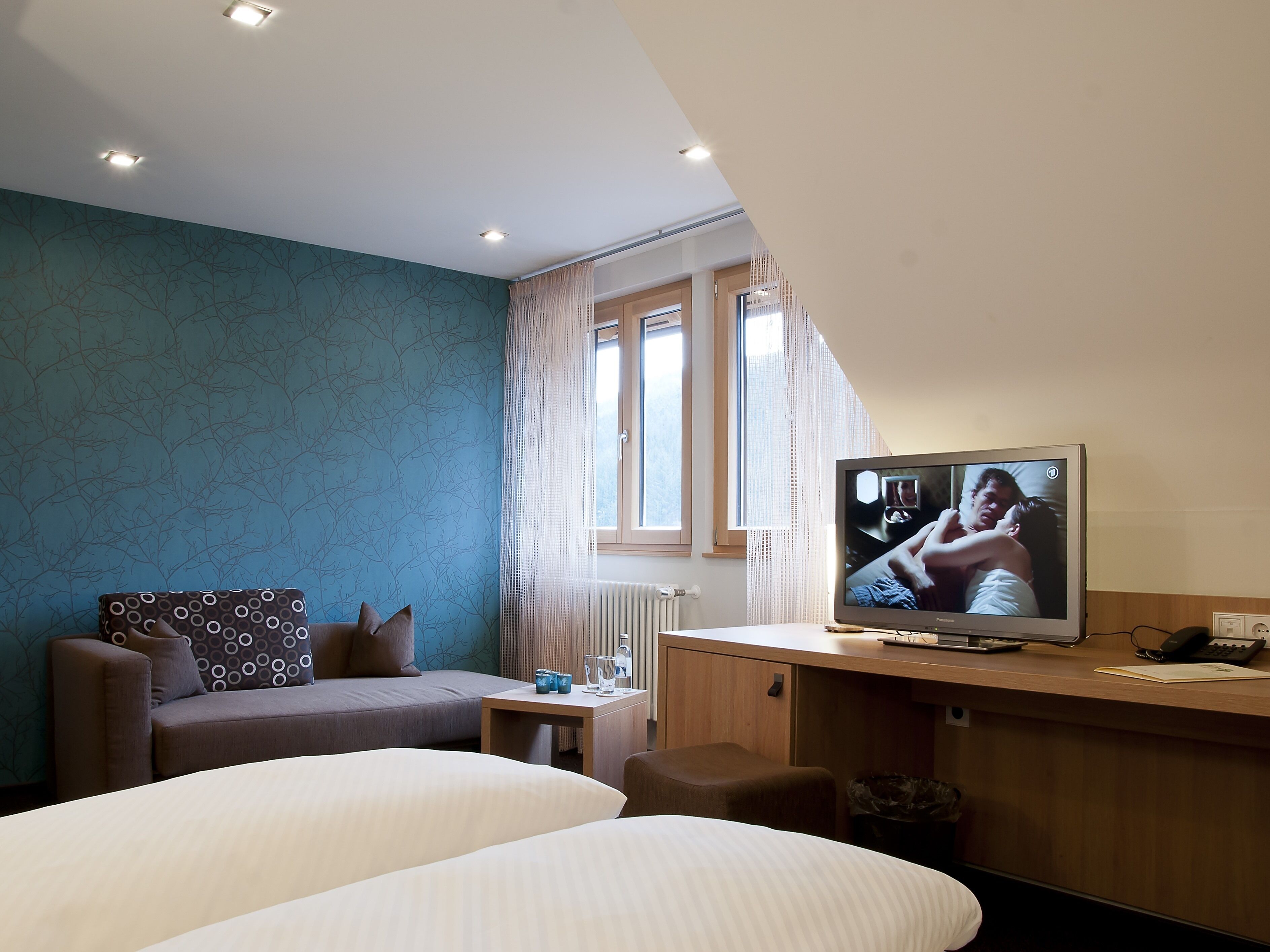A hotel room with a bed, a sofa, a desk, and a television displaying a movie scene.