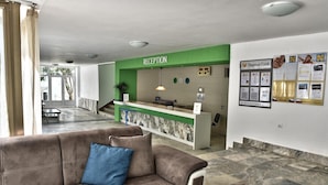 A reception area with a green counter, a brown sofa with a blue pillow, and a marble floor.