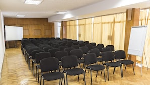 A conference room with rows of black chairs, a whiteboard, and a projector screen.