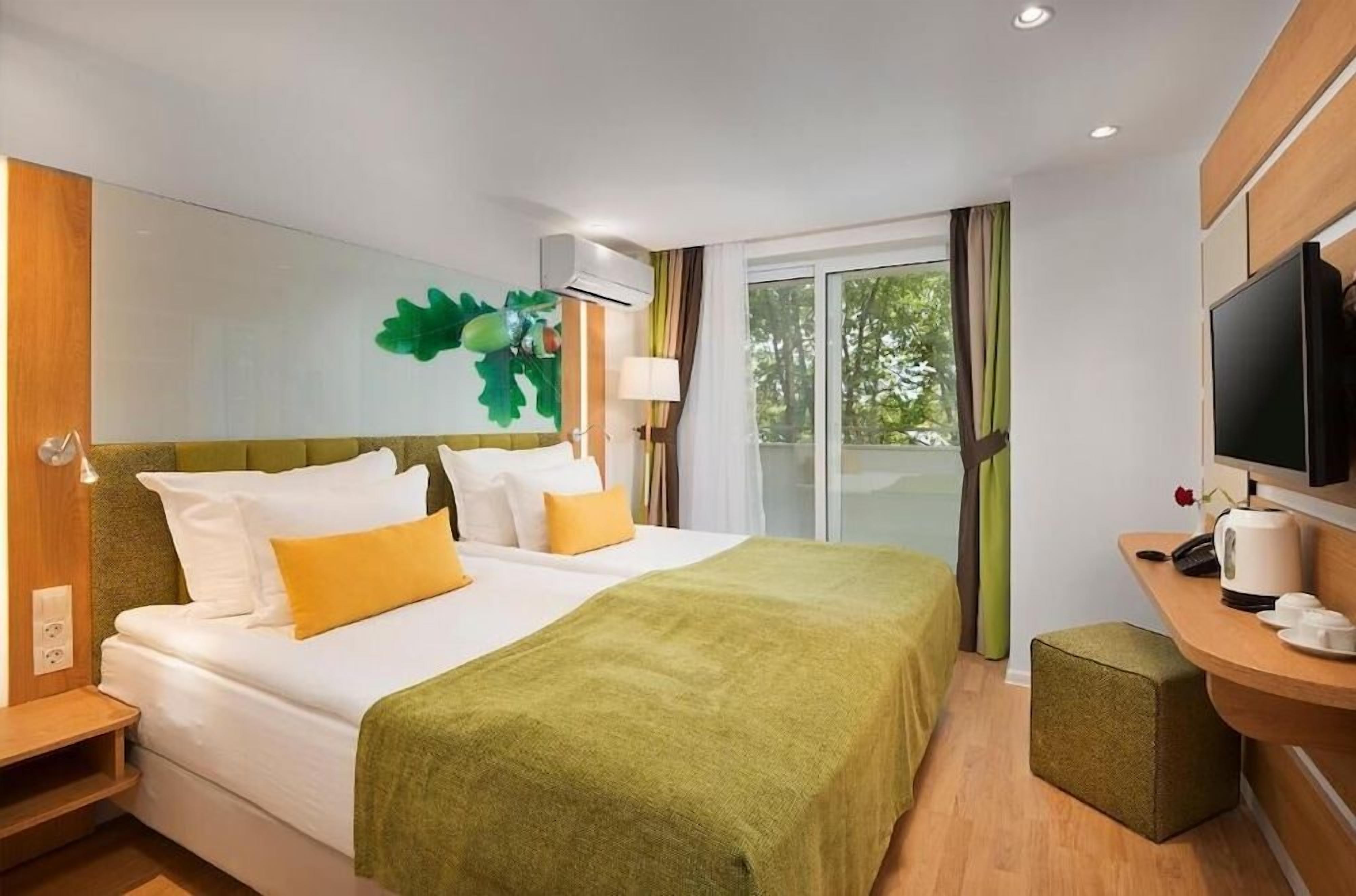 Ein Hotelzimmer mit einem Bett, einem Schreibtisch mit Kaffeemaschine, einem Fernseher und einem Fenster mit Vorhängen.
