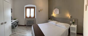 A hotel room with a bed, a desk, a radiator, and a window with curtains. - Hotel Mom Assisi (Assisi)