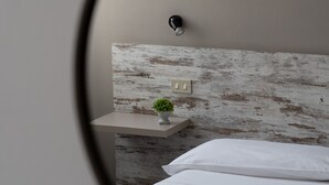 A bedroom with a bed, a bedside table with a plant, and a wall-mounted light fixture. - Hotel Mom Assisi (Assisi)
