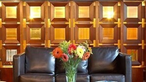 A lobby with a black leather sofa, a glass coffee table, and a vase of flowers. - Samaras Hotel (Lamia)