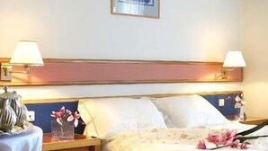 A hotel room with two beds, a nightstand with a lamp, a framed picture on the wall, and an air conditioning unit. - Samaras Hotel (Lamia)
