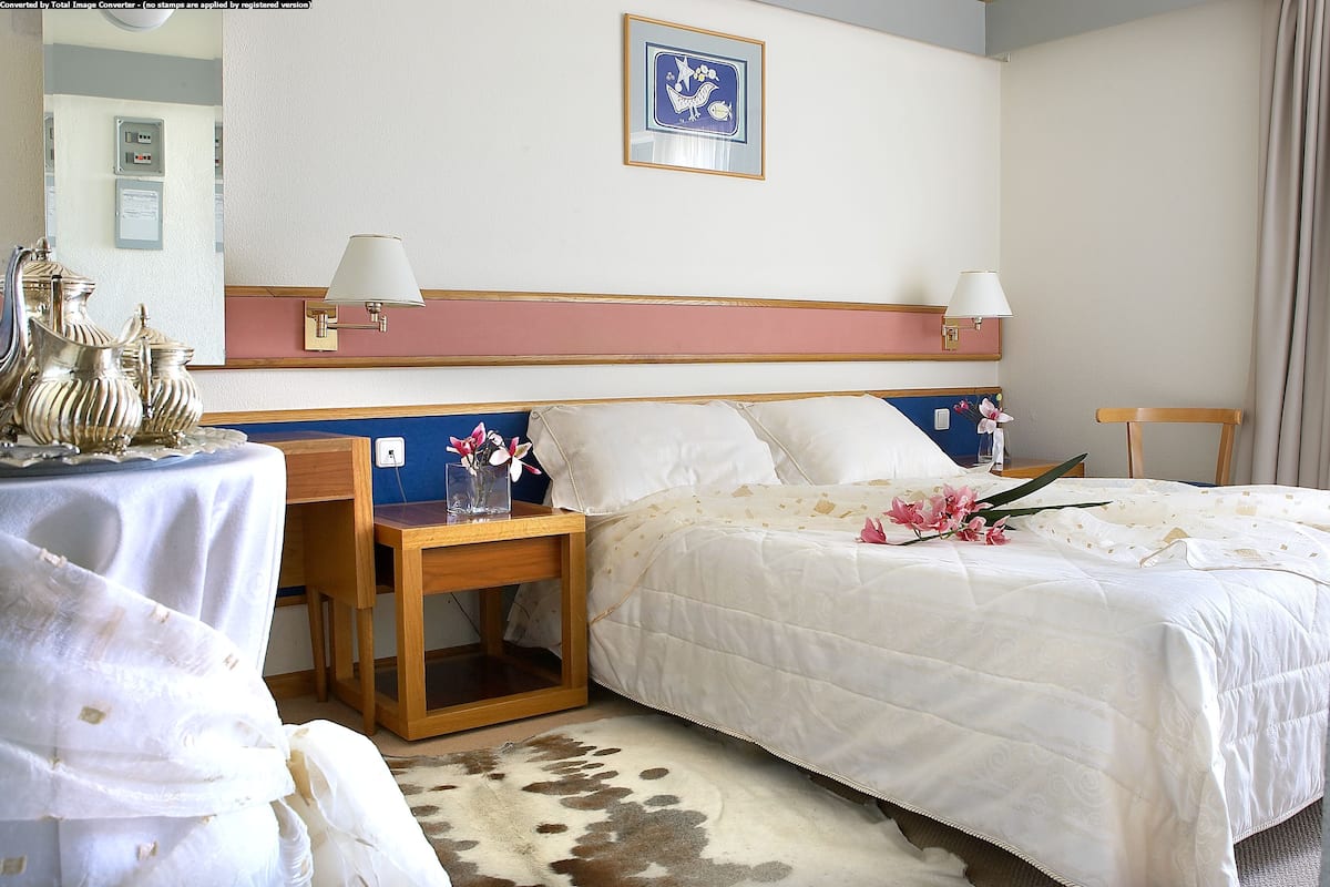 A hotel room with a bed, bedside tables, a mirror, a picture on the wall, and a small table with decorative items.