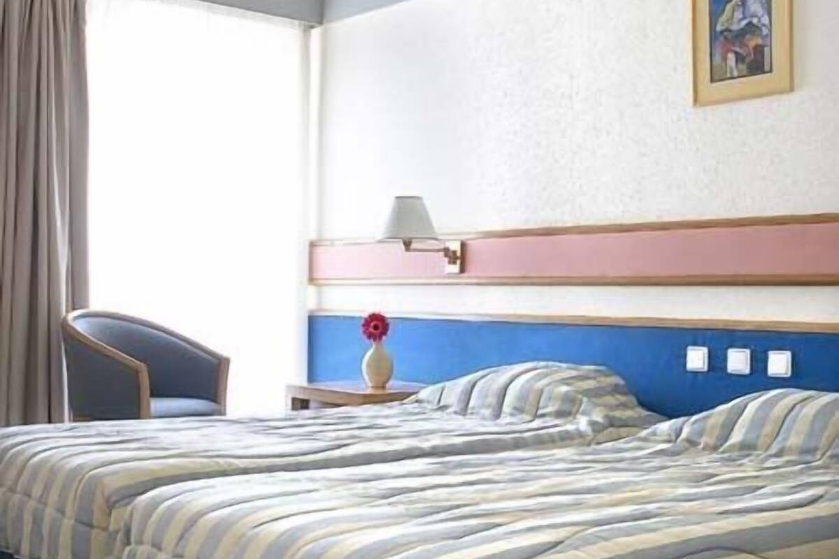 A hotel room with a bed, a chair, a nightstand, and a painting on the wall.