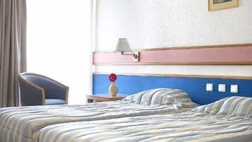 A hotel room with a bed, a chair, a nightstand, and a painting on the wall.