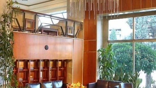 A lobby with leather sofas, a chandelier, and a wooden bookshelf. - Samaras Hotel (Lamia)