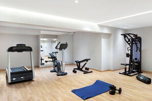 Ein Fitnessstudio mit Laufband, Crosstrainer, Bankdrücker und Kurzhantelbank.