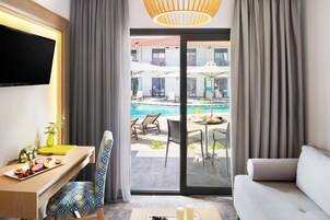 Quarto de hotel com televisão de tela plana, mesa de jantar com cadeiras, um sofá e vista para a área da piscina.