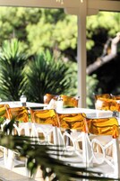 A table set with white chairs and amber glassware, number 36, in a covered outdoor area with greenery in the background.