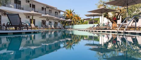 A pool area with lounge chairs and umbrellas, surrounded by a building with balconies and air conditioning units.