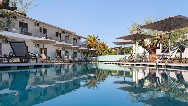 A pool area with lounge chairs and umbrellas, surrounded by a building with balconies and air conditioning units.