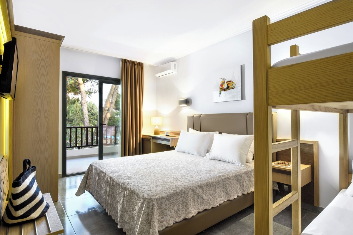 A hotel room with a bed, a desk, a chair, a window with curtains, and a balcony.