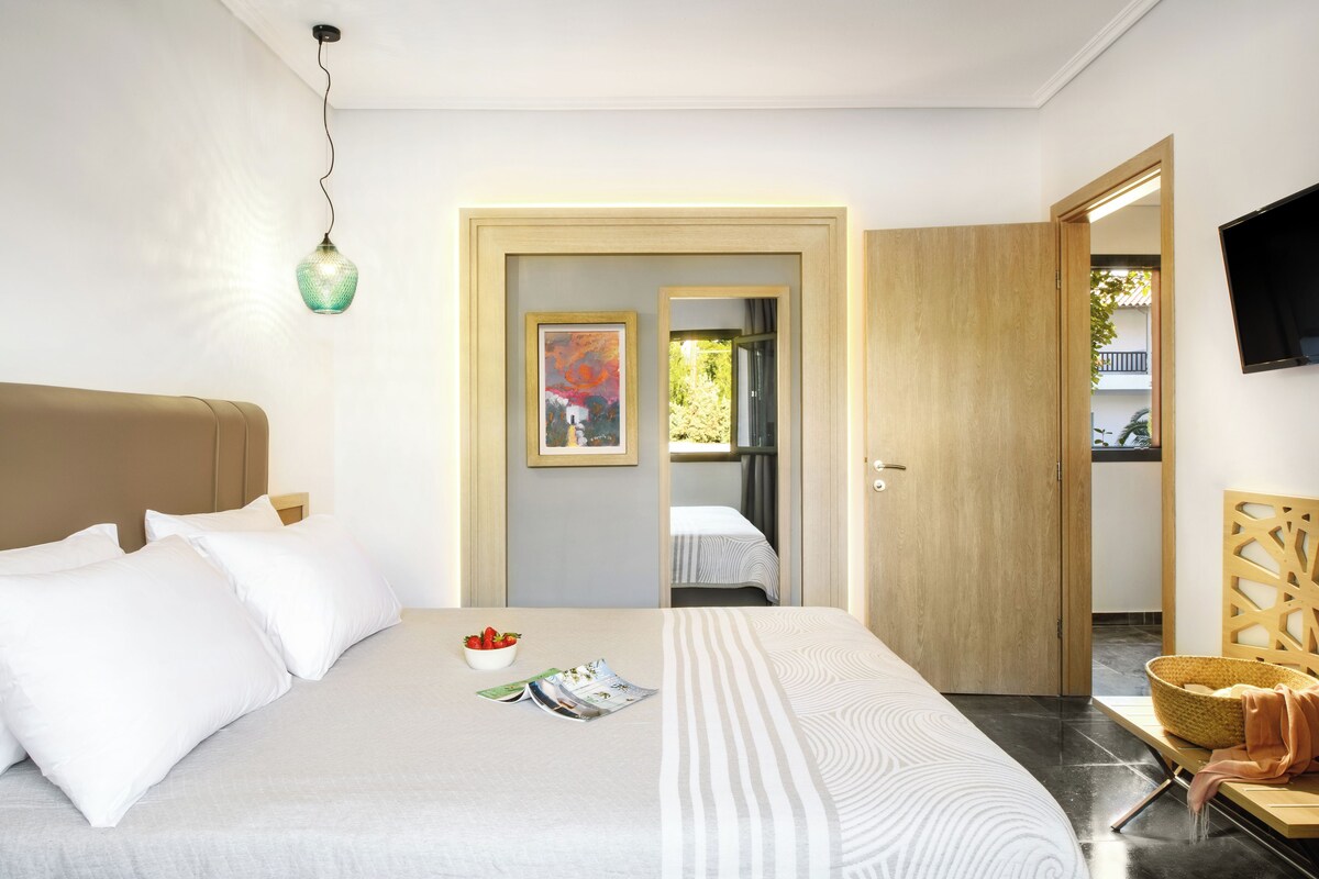 A modern hotel room with a large bed, a small table with a bowl of fruit, a magazine, and a painting on the wall.