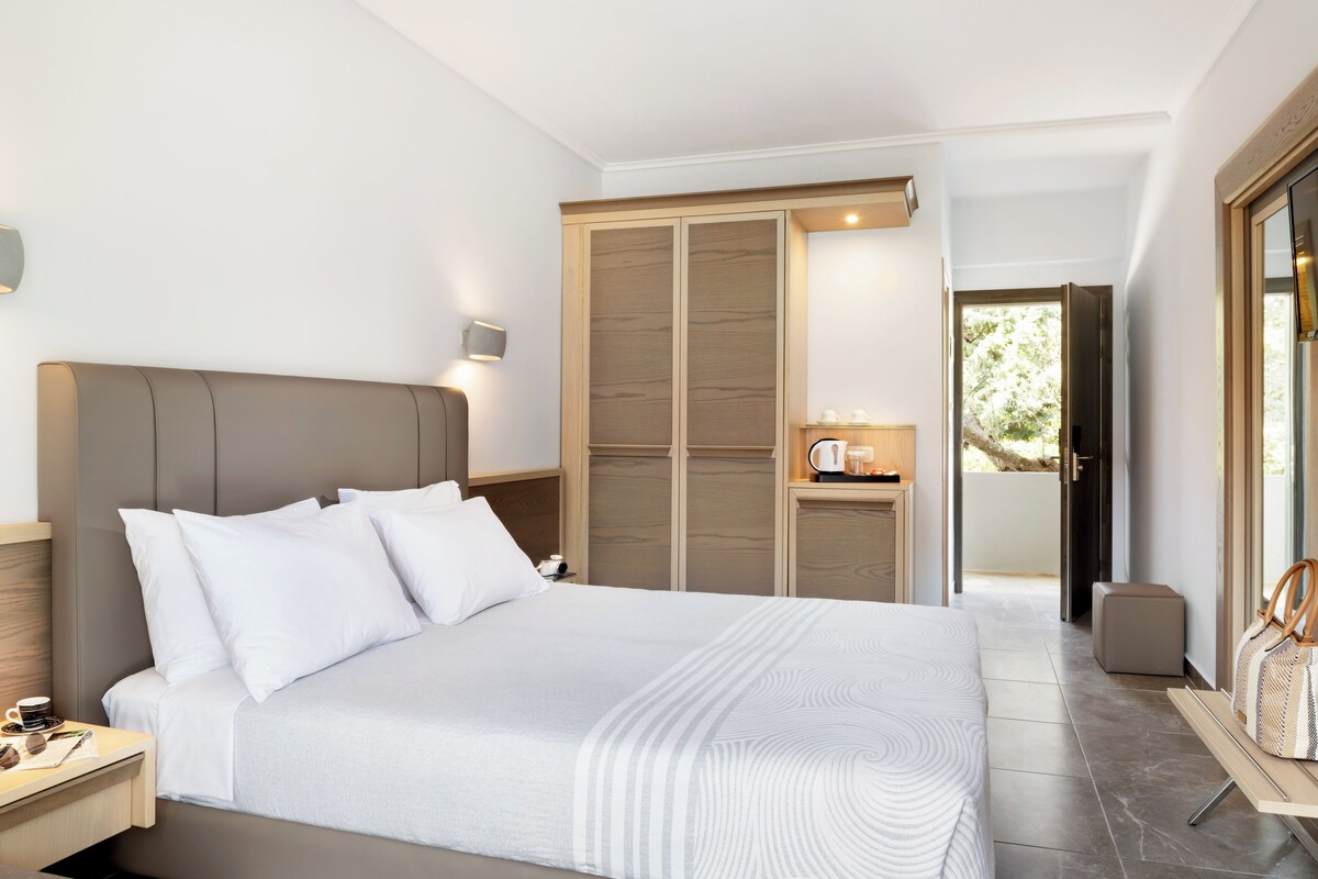 A modern bedroom with a large bed, a nightstand, a wardrobe, and a small table with a kettle.
