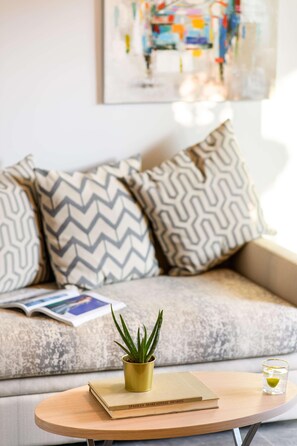 Ein Sofa mit gemusterten Kissen, ein kleiner Tisch mit einem Buch und einer Pflanze sowie ein Glas Wasser.