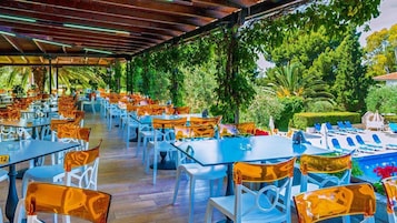 Zona de comedor al aire libre con mesas y sillas, rodeada de abundante vegetación y una piscina.