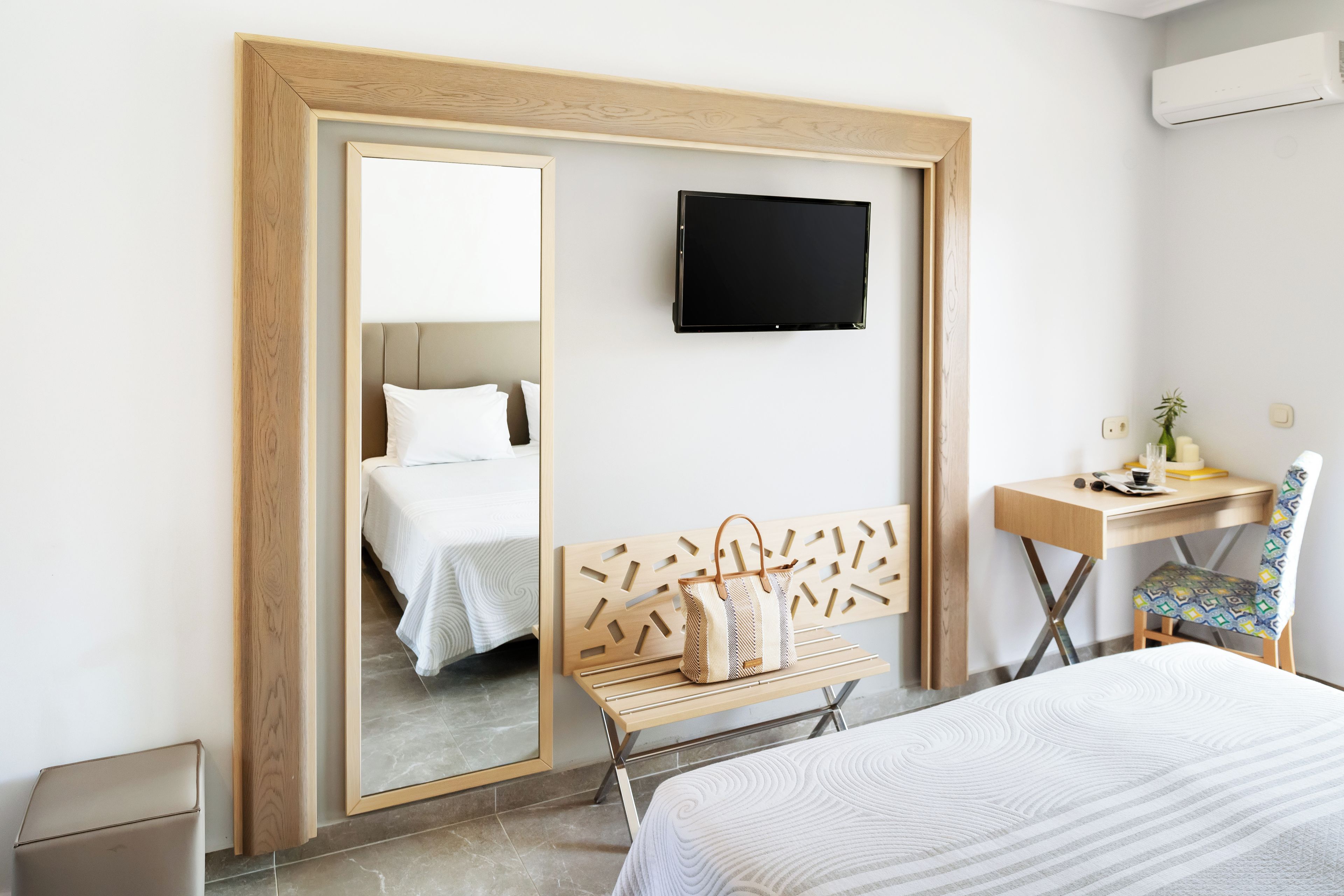 A hotel room with a bed, a desk, a chair, a television, and a mirror.