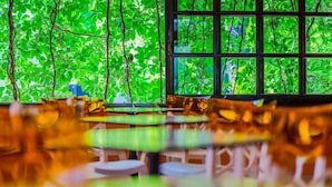 A dining area with tables and chairs, a large window with a view of green foliage. - Philoxenia Hotel (Polygyros)