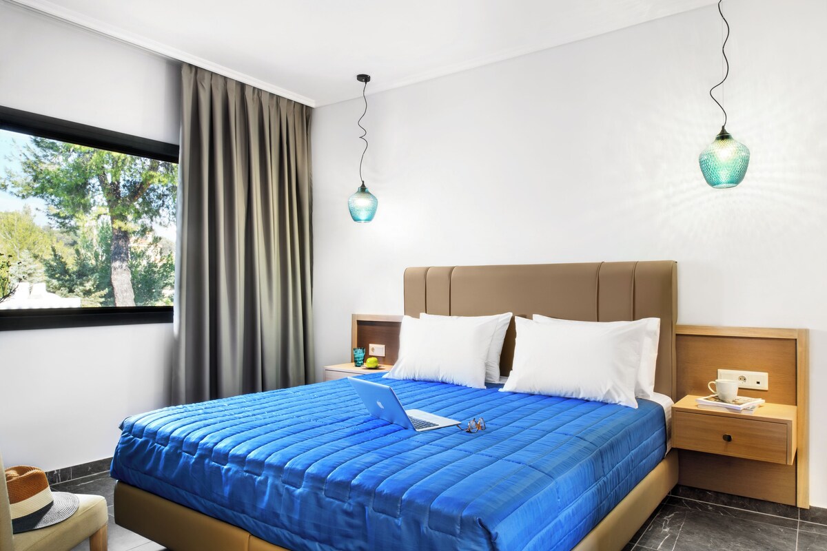 A hotel room with a large bed, a laptop, a nightstand, and a window with curtains.
