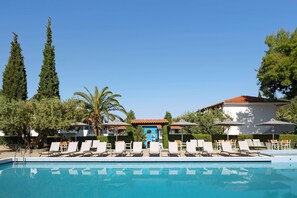 A swimming pool with lounge chairs and umbrellas, surrounded by trees and buildings. - Philoxenia Hotel (Polygyros)