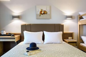 A hotel room with a bed, two bedside tables, a desk, a chair, a lamp, and a painting of a scooter.
