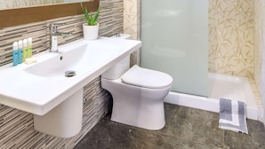 A bathroom with a white sink, mirror, and toilet, a shower with a glass door, and patterned walls.