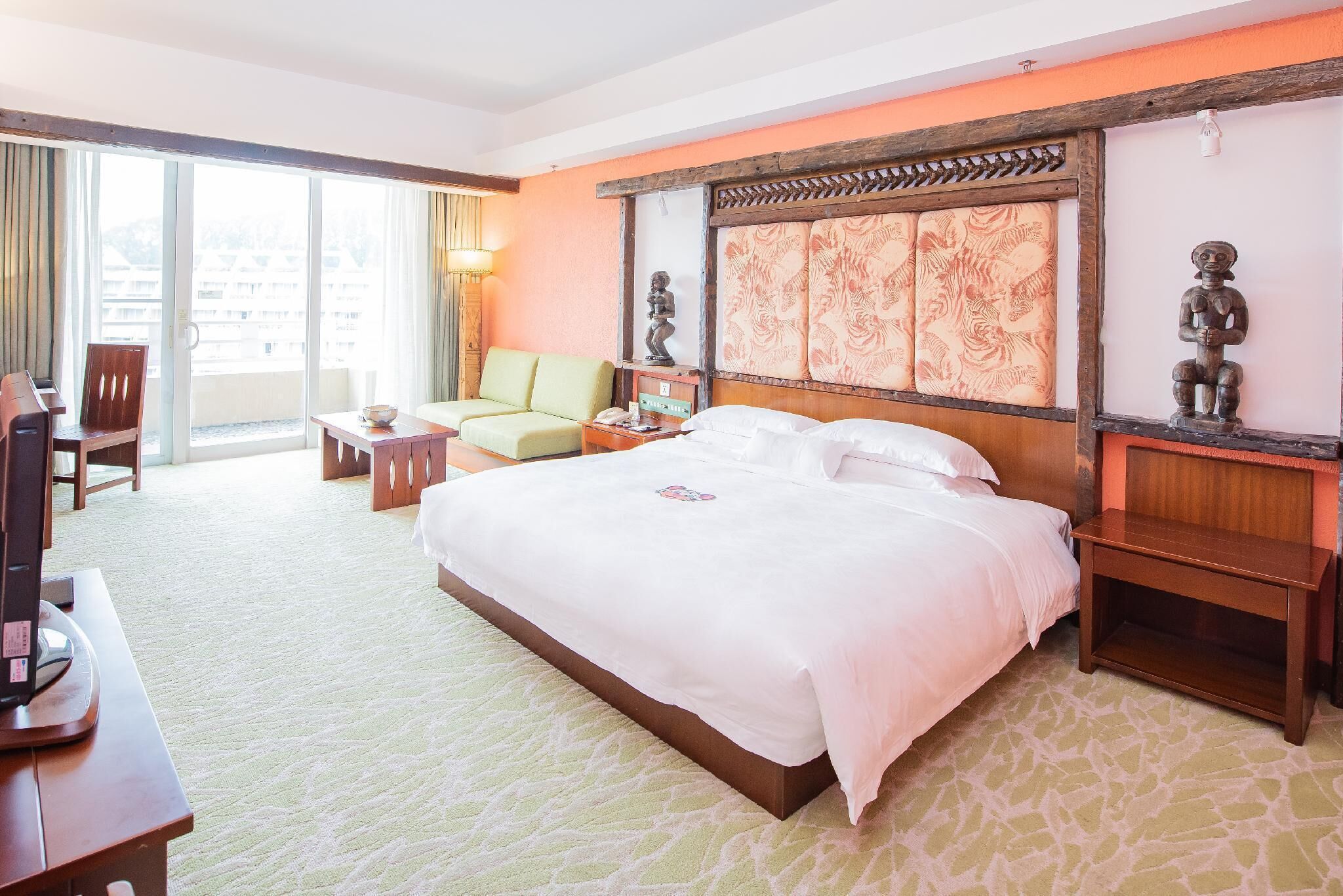A hotel room with a large bed, a sofa, a desk with a computer, and a view of the city through the window.